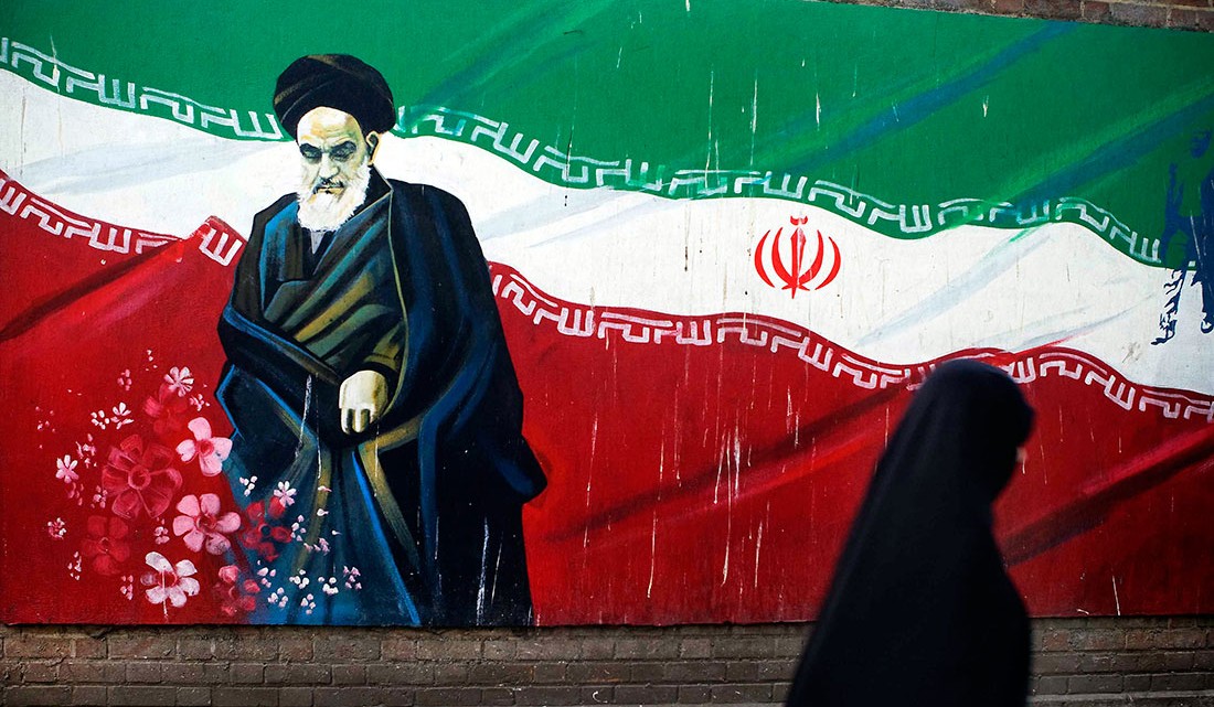 Mulher a passar junto a mural com Khomeini no Irão