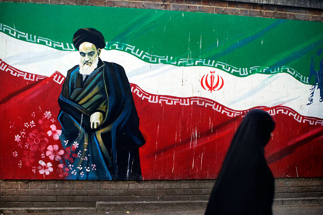 Mulher a passar junto a mural com Khomeini no Irão
