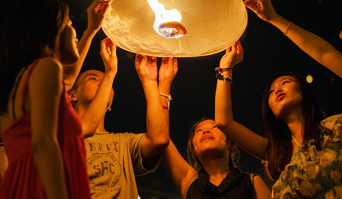 homens e mulheres tailandesas iluminados por um balão de ar quente durante o festival Loi Krathong