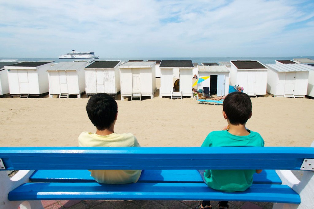 Crianças sentadas num banco junto à praia em Calais.