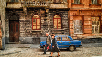 Casal a caminhar numa rua antiga de Lviv com Trabant azul estacionado