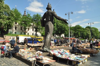 Feirinha de livros e antiguidades instalada junto a grande estátua numa praça de Lviv