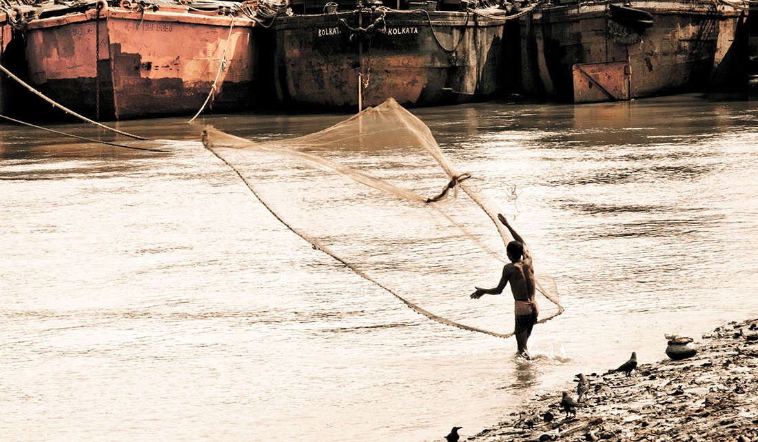 pescador a lançar as redes no rio Hooghly, em Calcutá, junto a estaleiro naval.