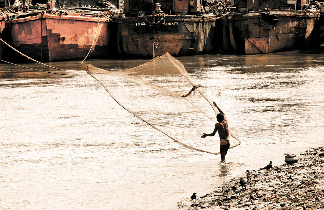 pescador a lançar as redes no rio Hooghly, em Calcutá, junto a estaleiro naval.