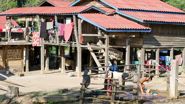 Criança a tomar banho na rua, junto às casas de madeira da vila de Muang Sing no Laos.