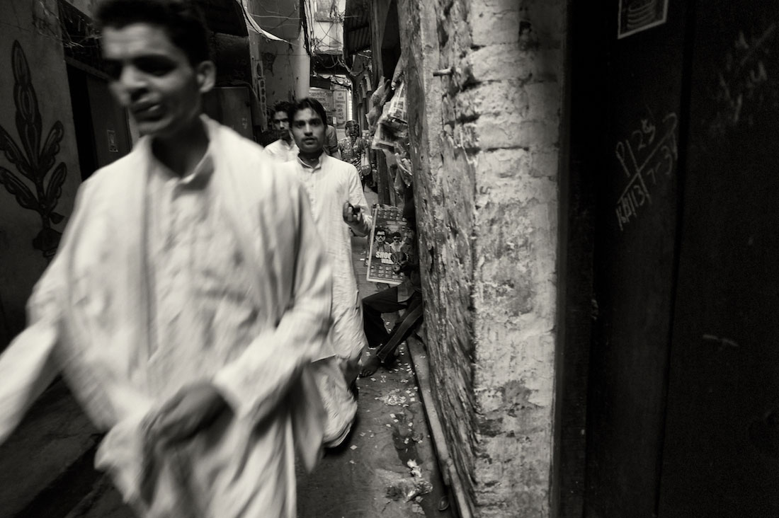 Homens vestidos de branco que passam numa ruela muito estreita de Varanasi antiga.