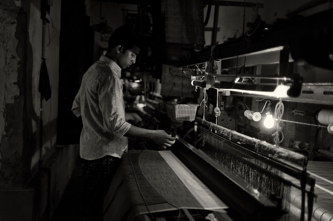 Rapaz a trabalhar com um tear numa pequena fábrica de tecidos em Varanasi.