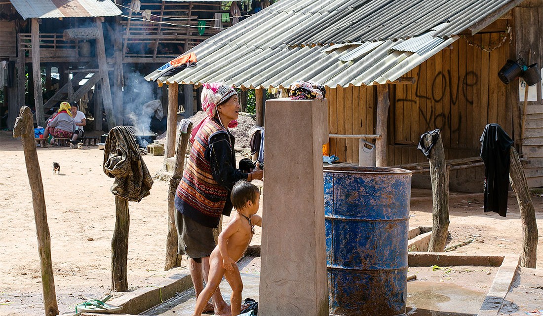 Mulher junto a fonte pública num largo da vila de Muang Sing.