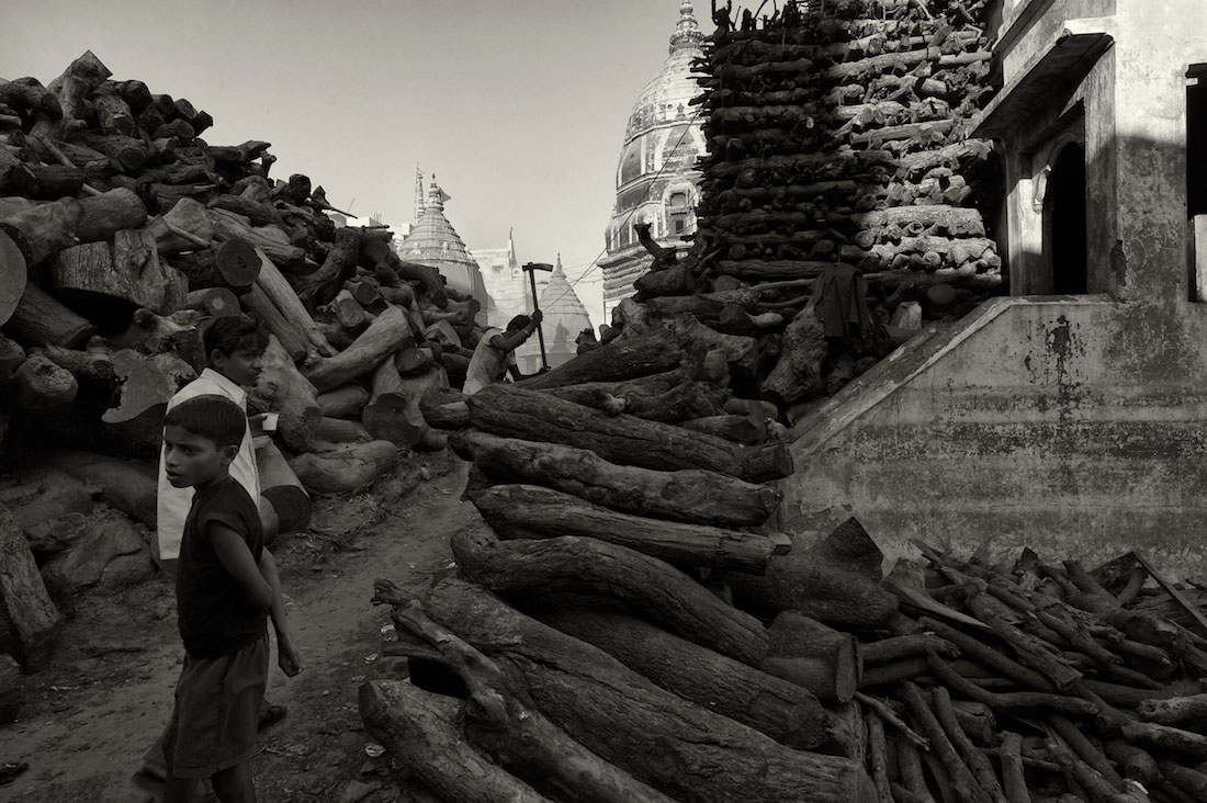 Crianças junto a montes de madeira para usar nas piras funerárias de Varanasi.