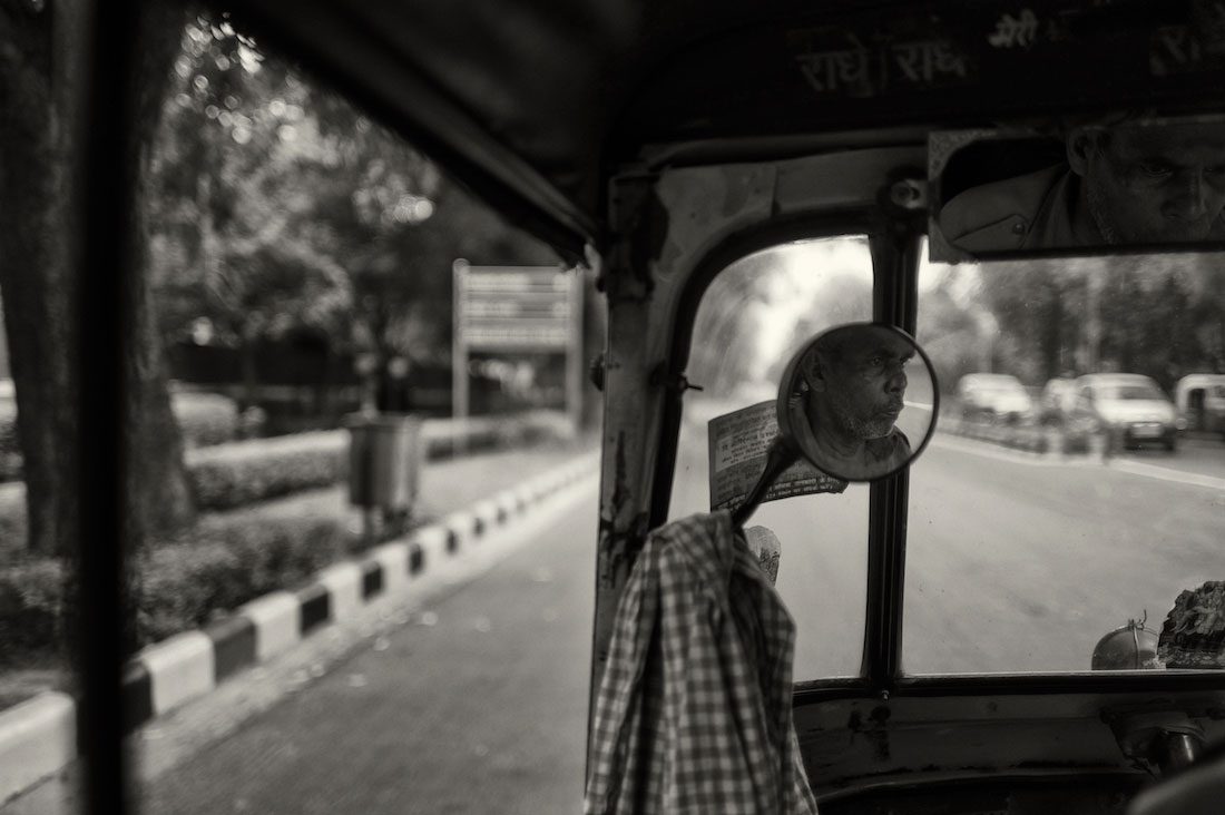 Reflexo de um condutor de rickshaw num espelho retrovisor.