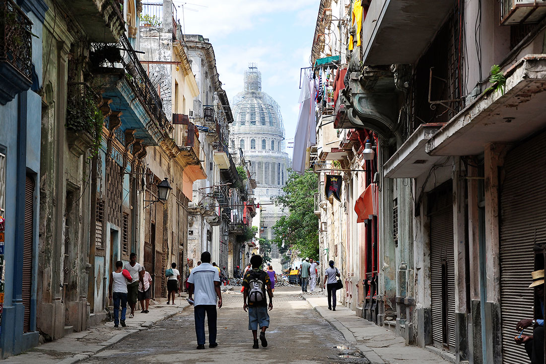 Pessoas numa rua de Havana Vieja com capitólio ao fundo.