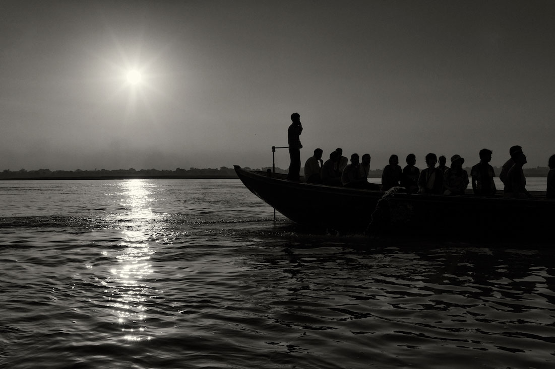 Silhueta de um barco cheio de turistas indianos, no rio Ganges, ao nascer do Sol.