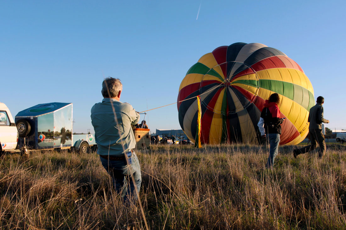 Balonista puxa grande balão colorido enquanto este se enche de ar quente.