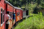 Comboio vermelho com pessoas penduradas a atravessar a montanha no centro do Sri Lanka até a cidade de Ella.