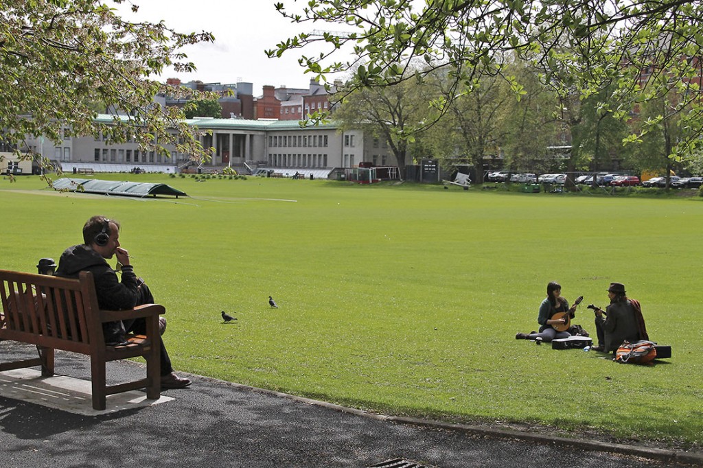 Homem sentado e dois músicos no relva verde dos jardins do Trinity College em Dublin.