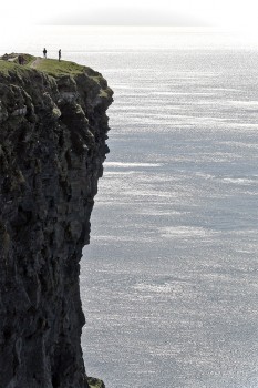 Duas pessoas junto à berma de um grande penhasco dos Cliffs of Moher.