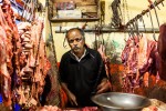 Homem talhante com muita carne pendurada em ganchos de um talho no mercado de Nuwara Eliya no Sri Lanka.