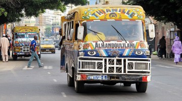 Autocarros coloridos e pessoas nas ruas de Dakar, Senegal.