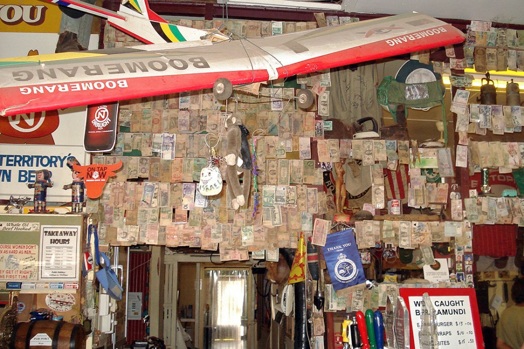 Notas de vários países e avião agarrados a uma das paredes do interior do Daly Waters Pub.