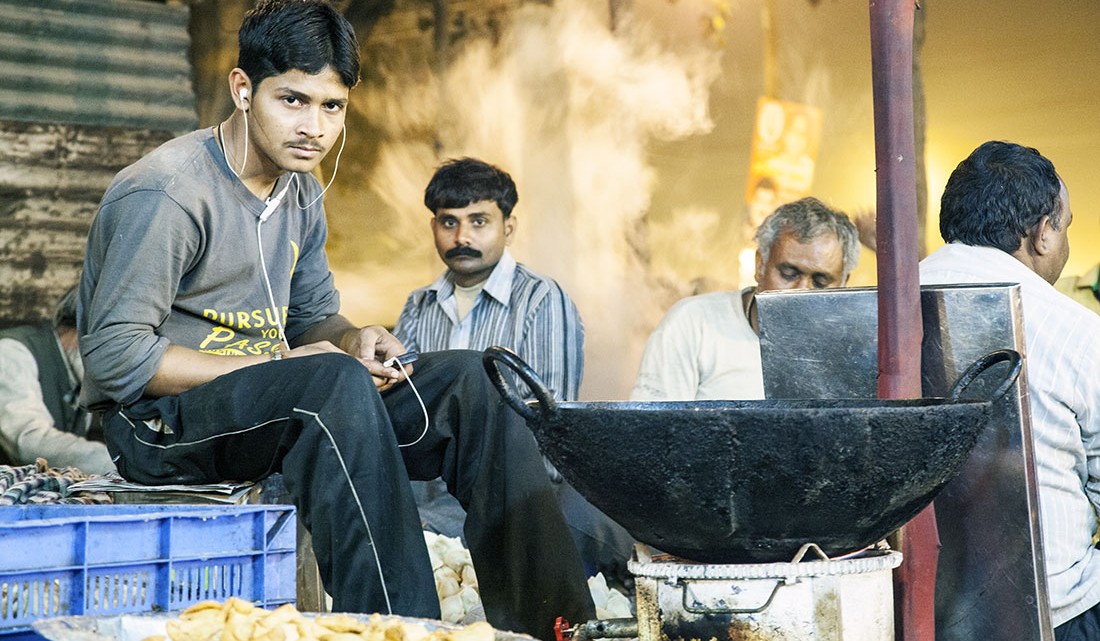 Rapaz a ouvir musica numa banca para comer na rua, Índia.