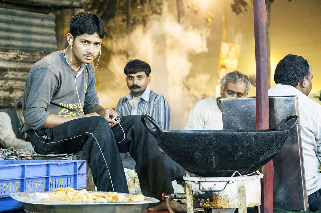 Rapaz a ouvir musica numa banca para comer na rua, Índia.