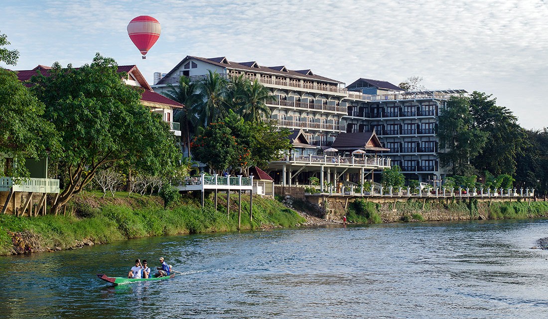 Hotel e balão de ar quente junto ao rio Nam Song, onde navega uma canoa, na cidade de Vang Vieng, Laos.