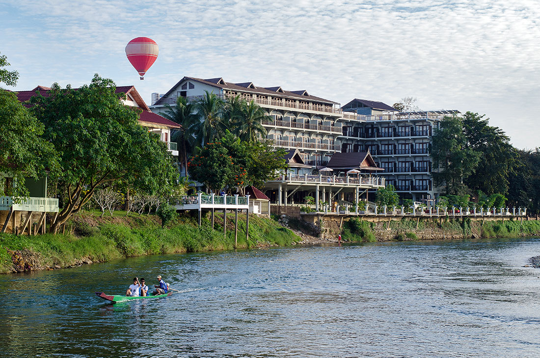 Hotel e balão de ar quente junto ao rio Nam Song, onde navega uma canoa, na cidade de Vang Vieng, Laos.