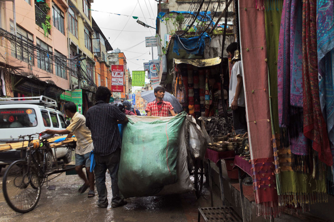Numa das ruas de Kathmandu procede-se à descarga de um grande saco com mercadoria para vender.