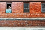 Homem Hindu espreita por uma janela de um prédio de tijolo em Kathmandu.