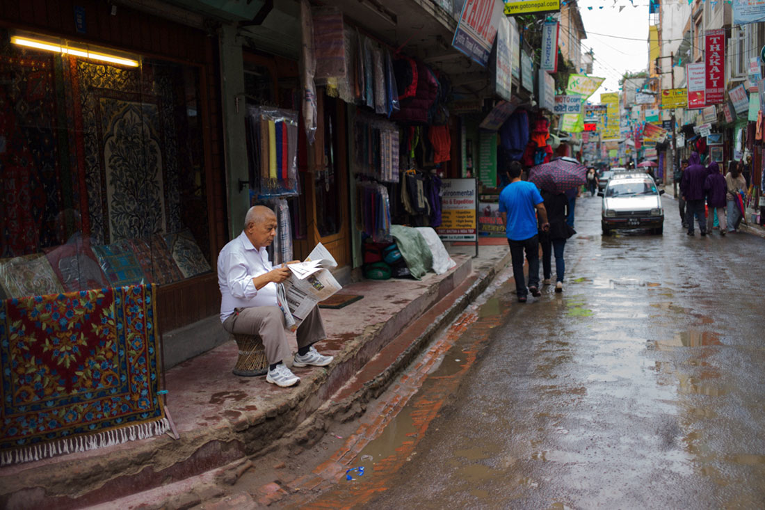 Vendedor de tapetes a ler jornal frente à sua loja em Kathmandu.