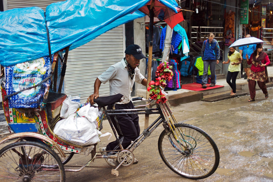 Homem conduz o seu riquexó à mão cheio de mercadoria para venda.