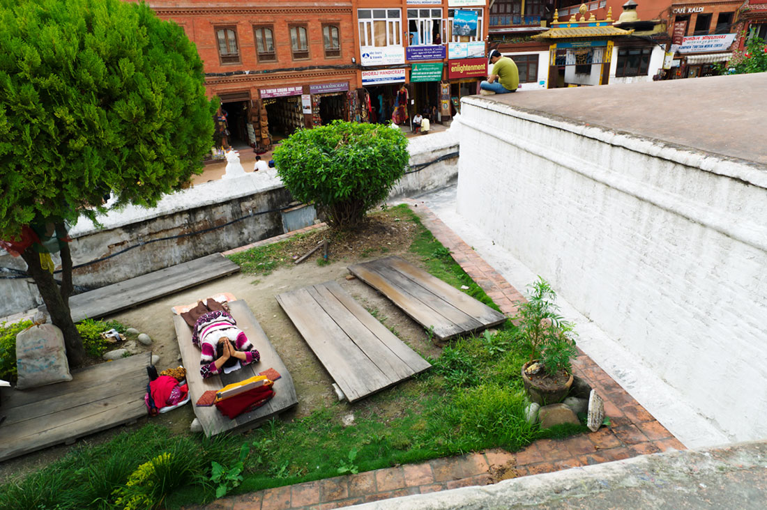 Mulher reza em pequeno jardim junto a um dos muros laterais da Boudhanath Stupa em Kkathmandu.