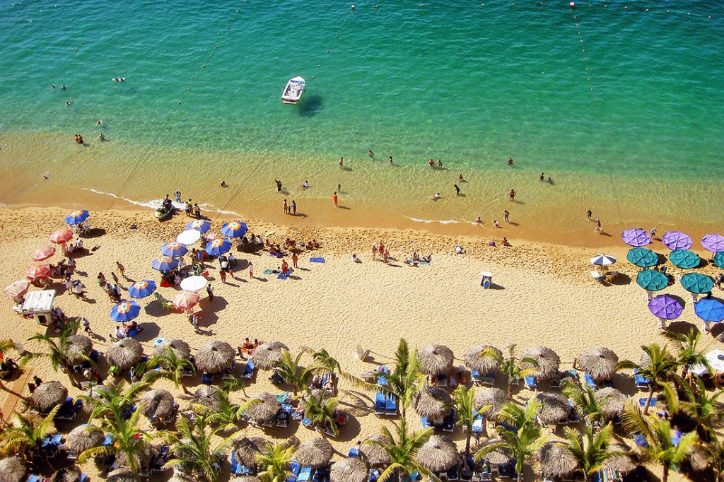 Praia em Acapulco cheia de chapéus-de-sol e águas verde-esmeralda.