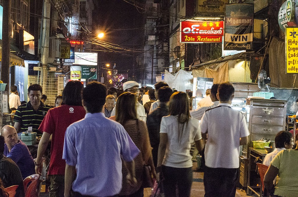 Grande movimento de pessoas a circular numa rua de Yangon, já durante a noite.