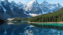 Montanhas com neve reflectidas nas águas de um lado do Parque Nacional Waterton, parte das Rocky Mountains no Canadá.
