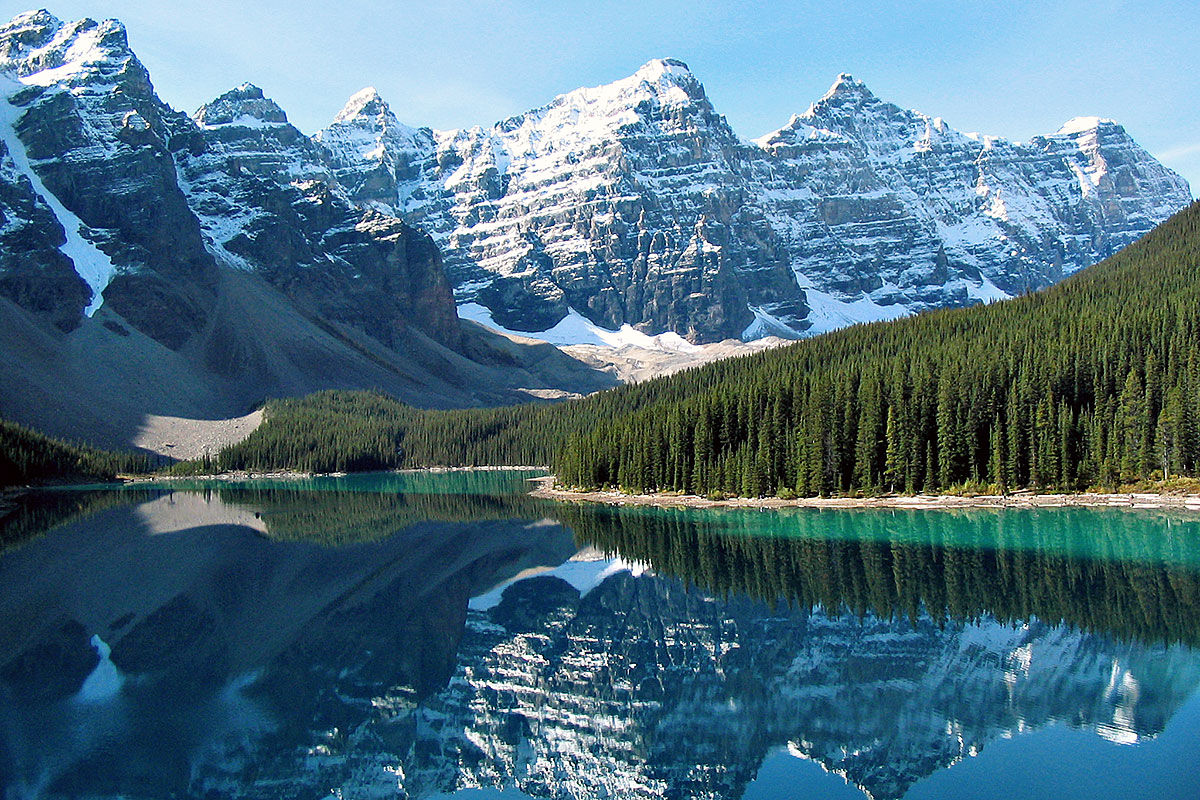 Montanhas com neve reflectidas nas águas de um lado do Parque Nacional Waterton, parte das Rocky Mountains no Canadá.