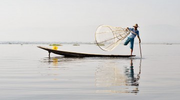 Pescador sobre a sua canoa a pescar com artes de pesca tradicionais do lago Inle, em Myanmar.