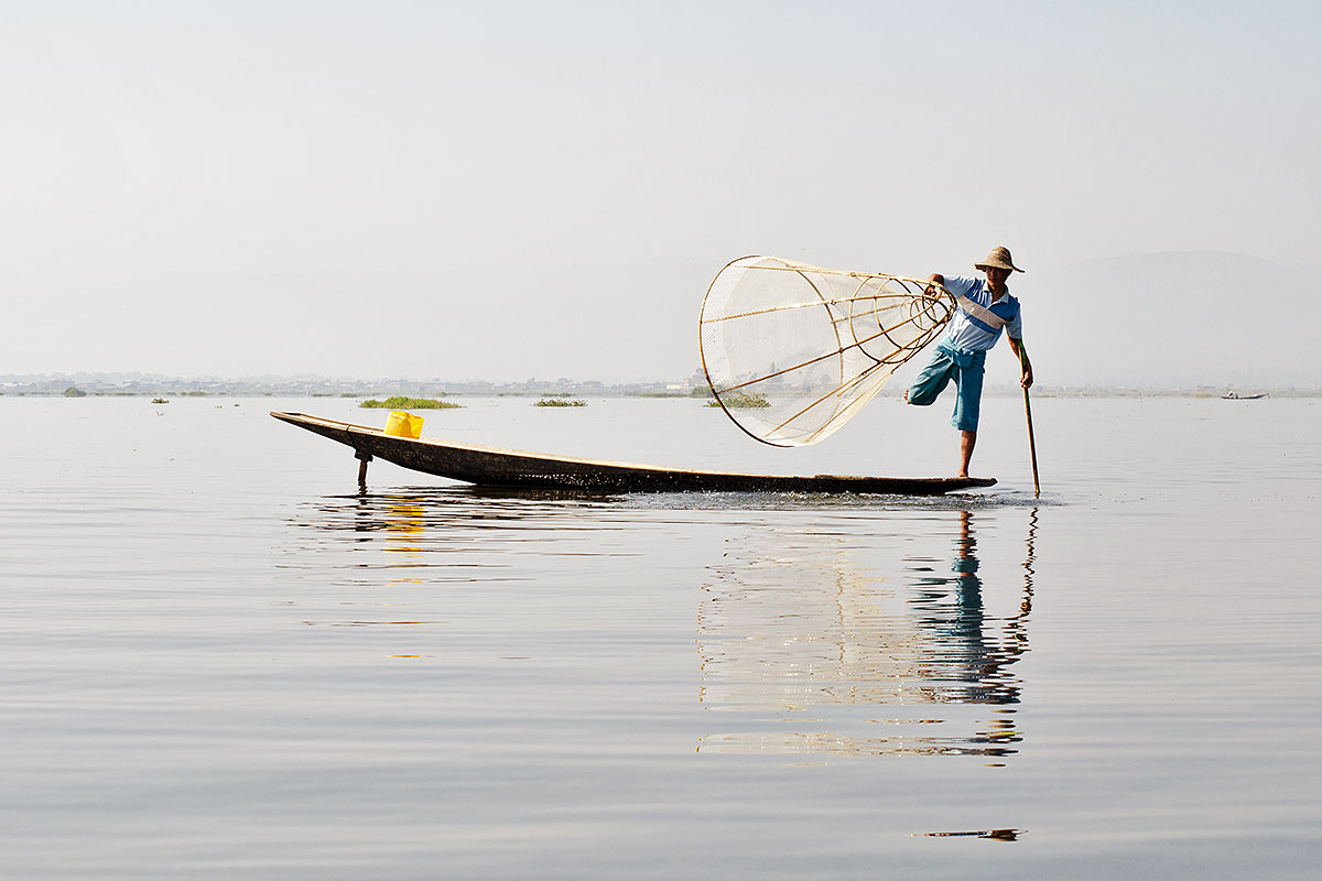 Pescador sobre a sua canoa a pescar com artes de pesca tradicionais do lago Inle, em Myanmar.