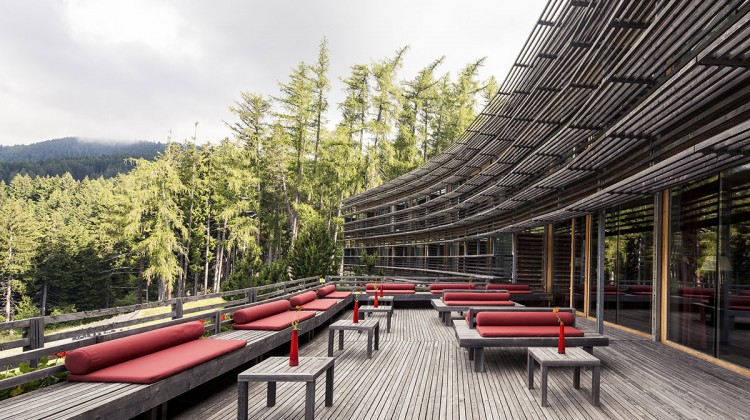 Bancos e mesas no terraço de madeira do Vigilius Mountain Resort virado para a montanha.