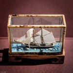 Maquete de barco dentro de uma vitrina de vidro e madeira.